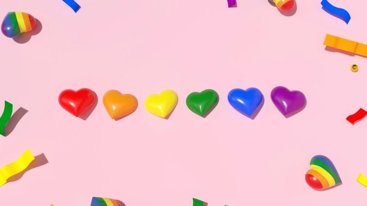 Heart shaped beads in rainbow colors on plain pink background.